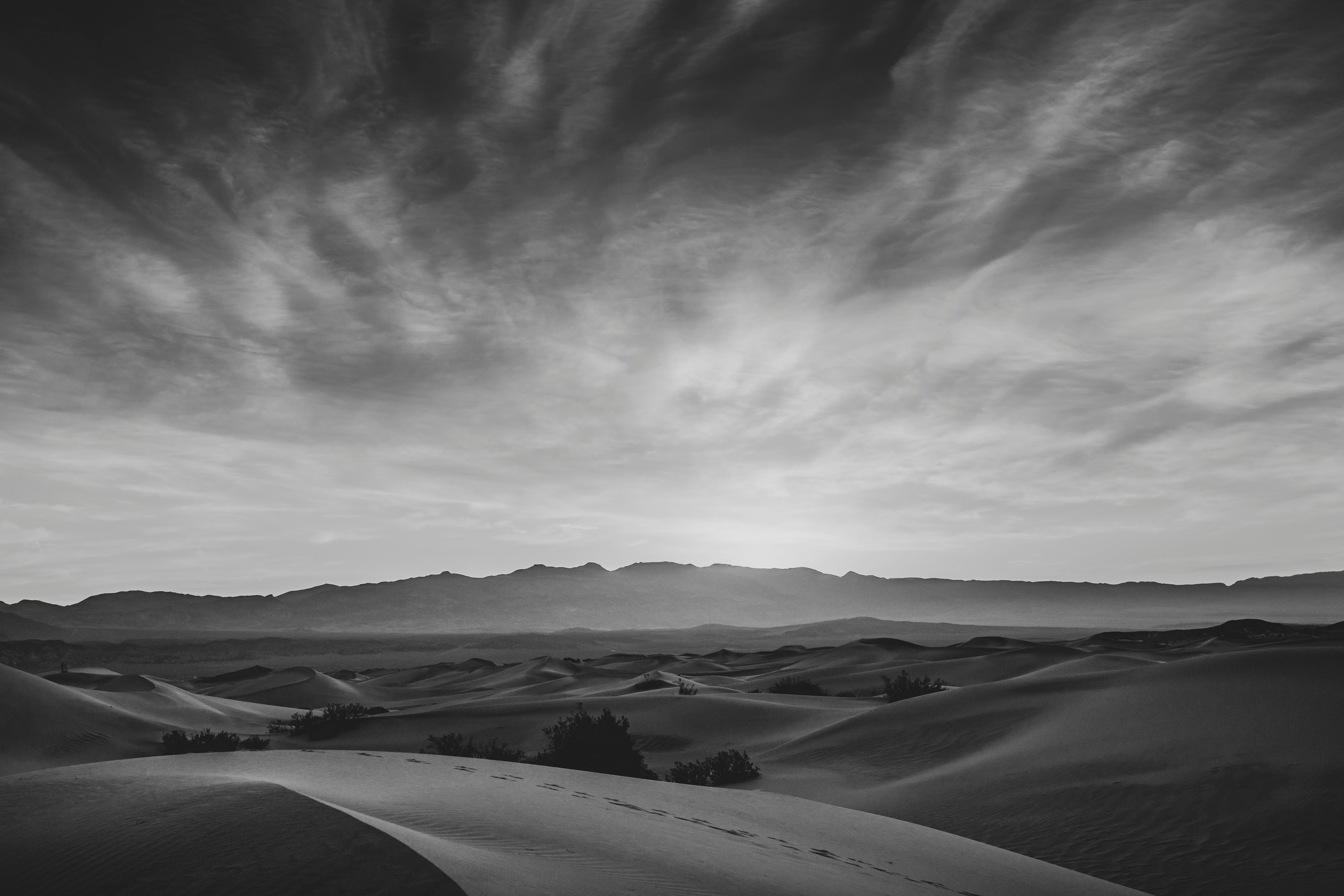 Stunning black and white capture of desert dunes at twilight with dramatic clouds.