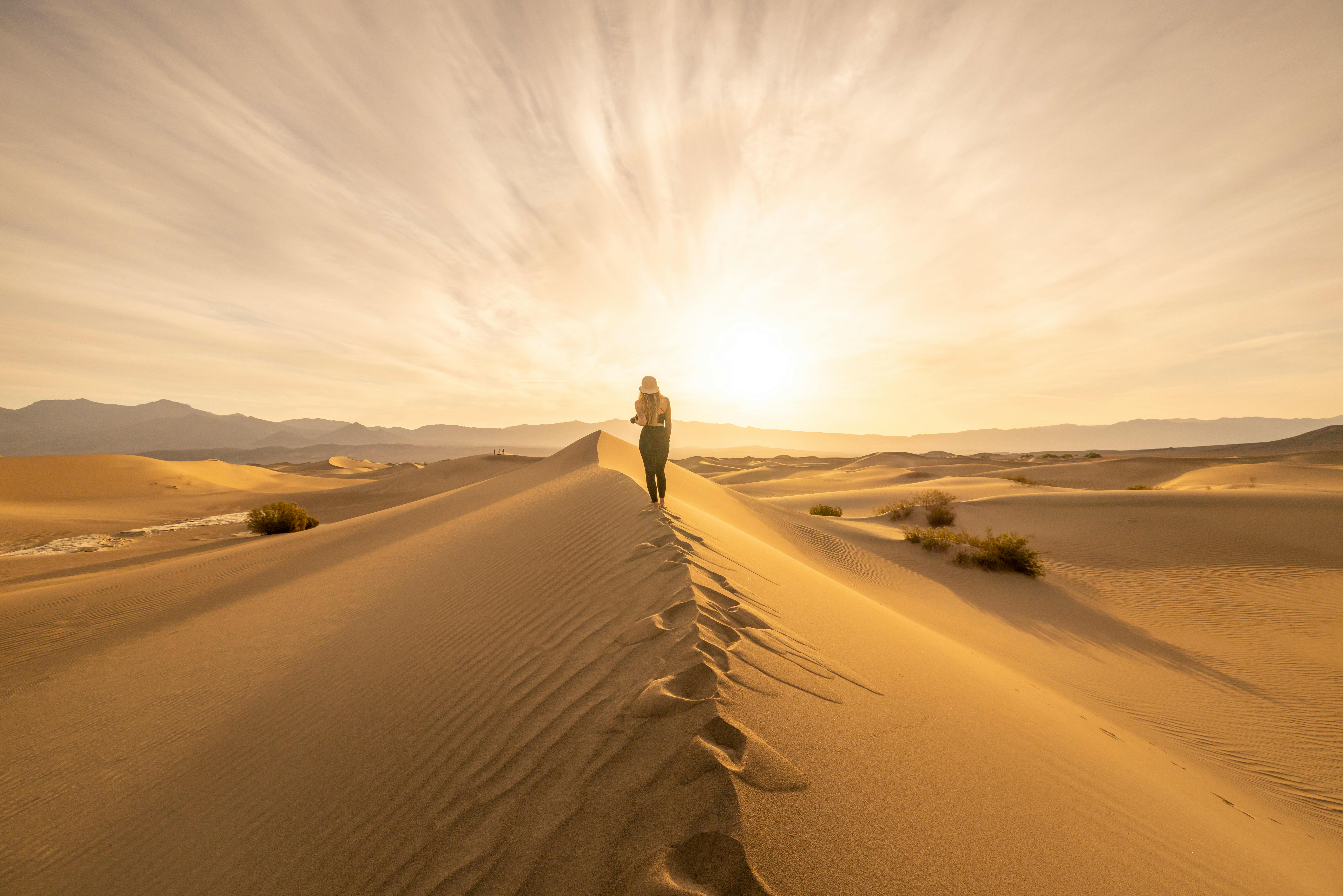 Captivating image of a lone woman walking along the sunlit desert sand dunes at sunrise.