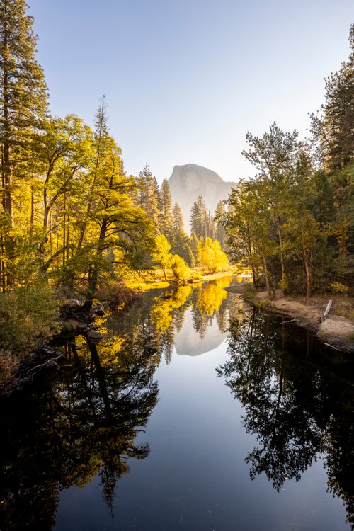 Free Scenic view of Yosemite's Half Dome with lush trees reflected in a tranquil river. Stock Photo
