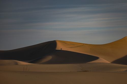 Free A serene view of vast sand dunes with people silhouetted at twilight. Stock Photo
