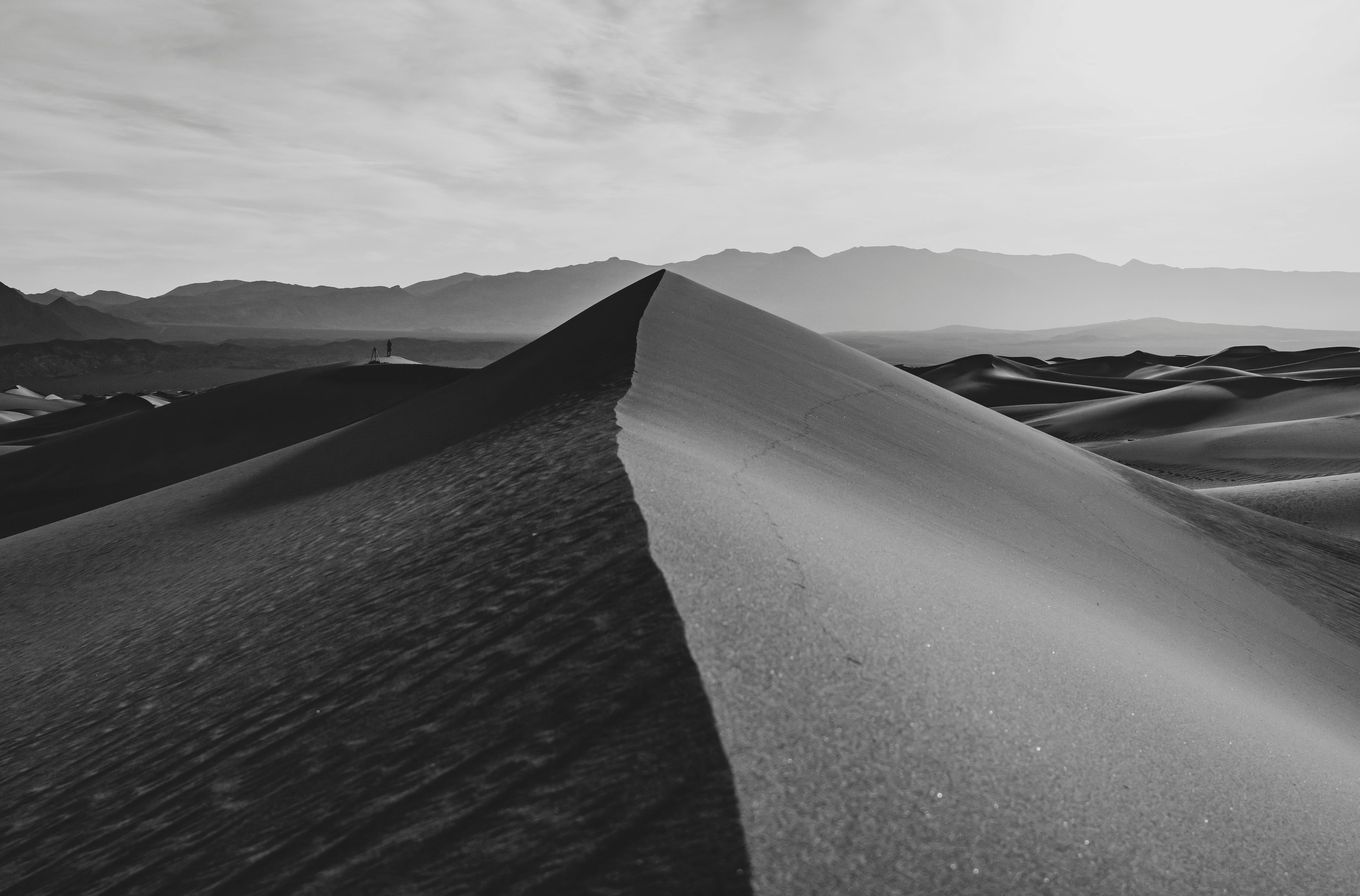 Monochrome image of sand dunes with mountains in the background, creating a serene desert scene.