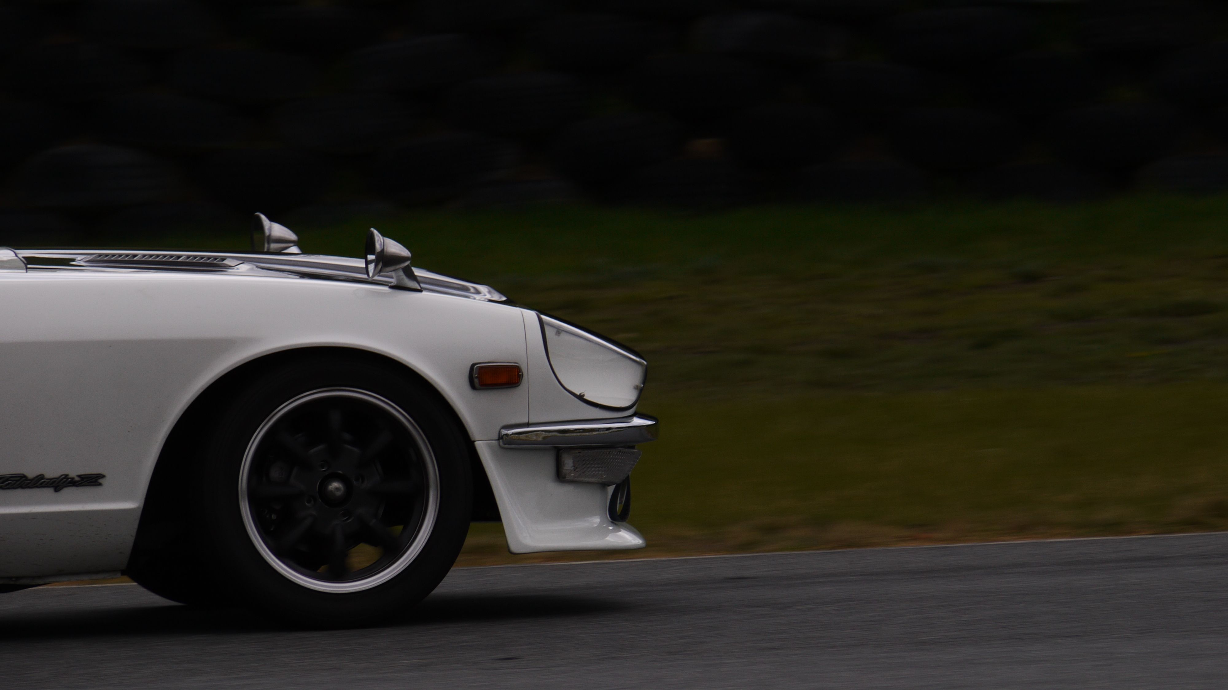 Side view of a classic white 1970s sports car driving on a scenic road.