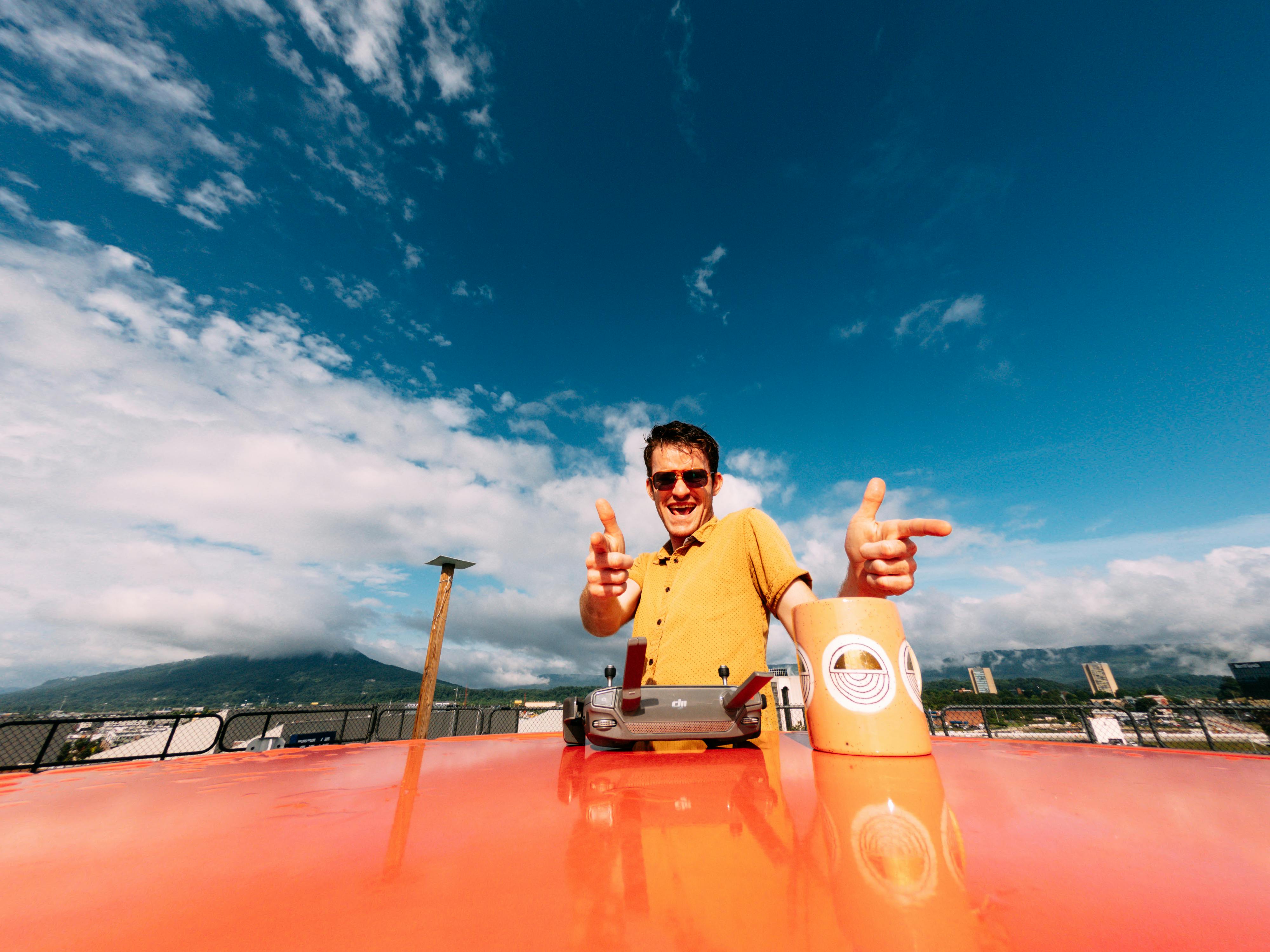 一名快乐的男子戴着太阳镜，在充满活力的蓝天下，开玩笑地对着无人机控制器摆姿势