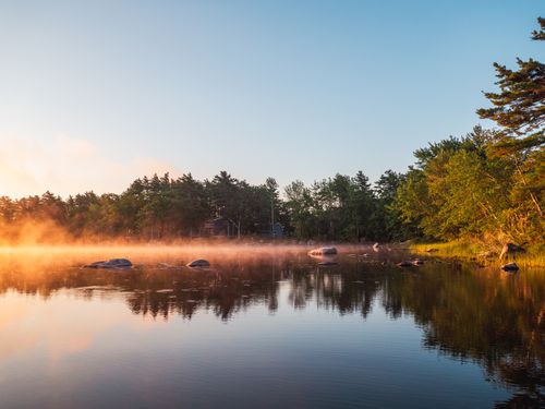 Free Tranquil lake scene with mist at sunrise reflecting trees in clear water. Stock Photo