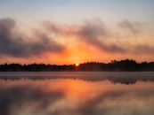 Peaceful sunrise over a calm lake with mist and vivid reflections.