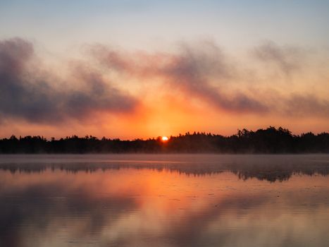 Peaceful sunrise over a calm lake with mist and vivid reflections.