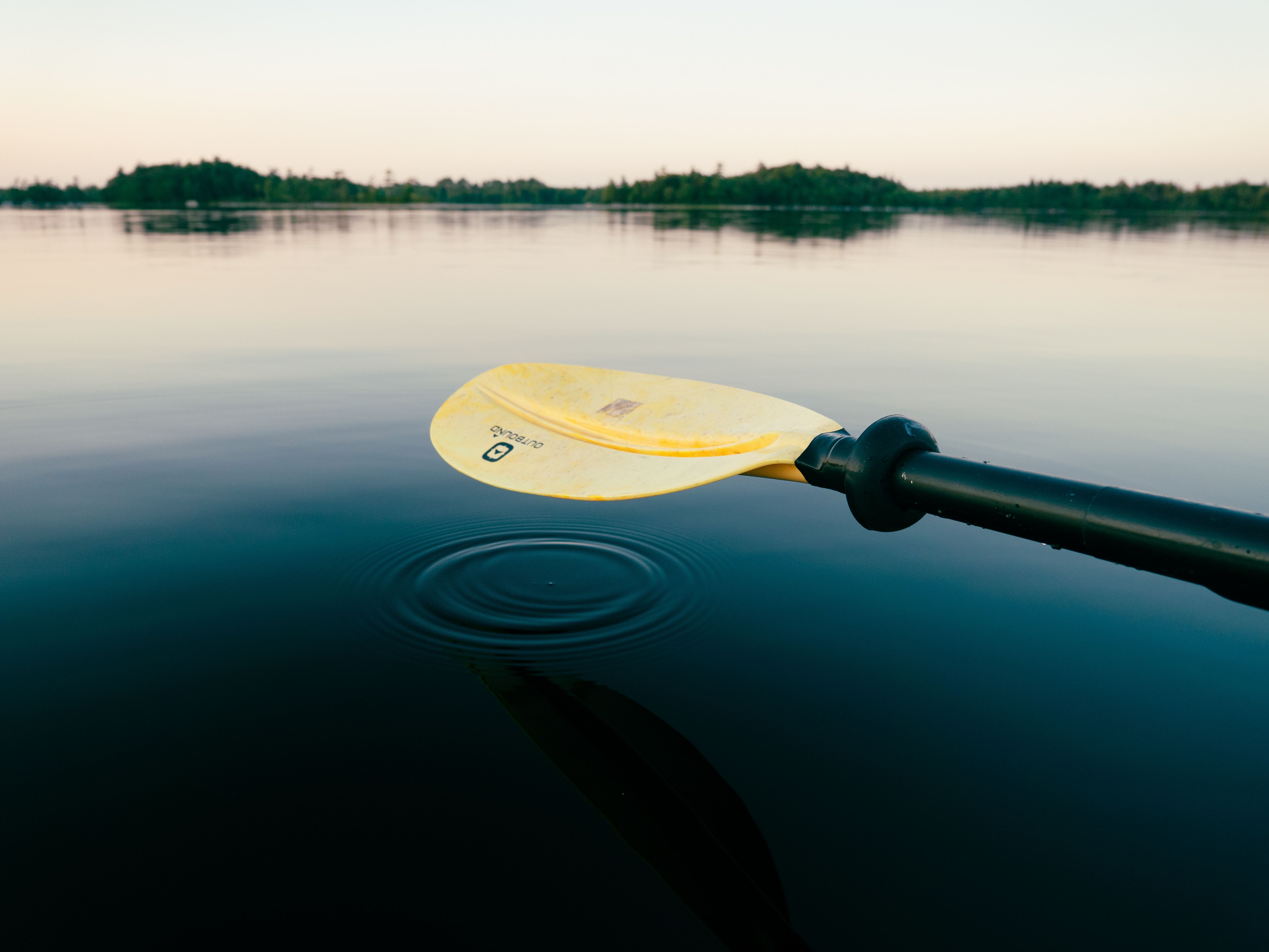 A tranquil scene of a kayak paddle resting on calm lake waters at twilight.