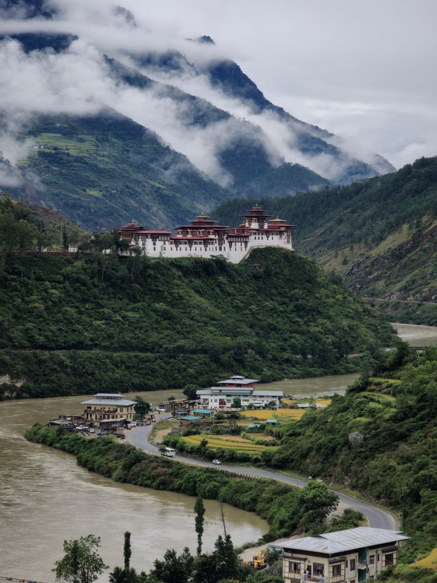 Vale de Punakha coberto de floresta, com nuvens baixas e um dzong ao fundo