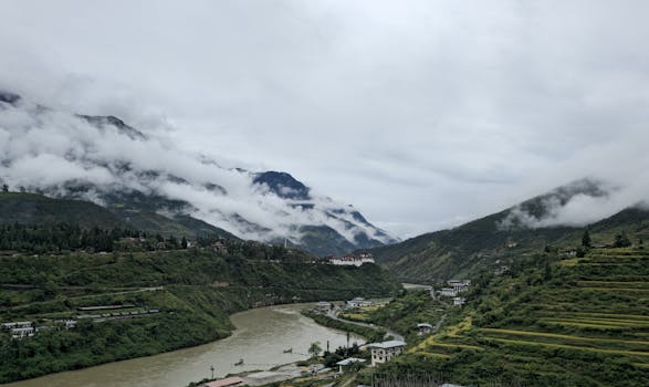 A breathtaking view of Wangdue Phodrang's lush greenery and river under cloud-kissed mountains.