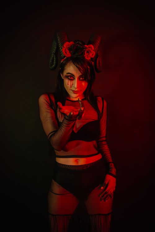 Free Woman dressed in mystical attire with horns and red lighting. Fantasy and Halloween theme. Stock Photo