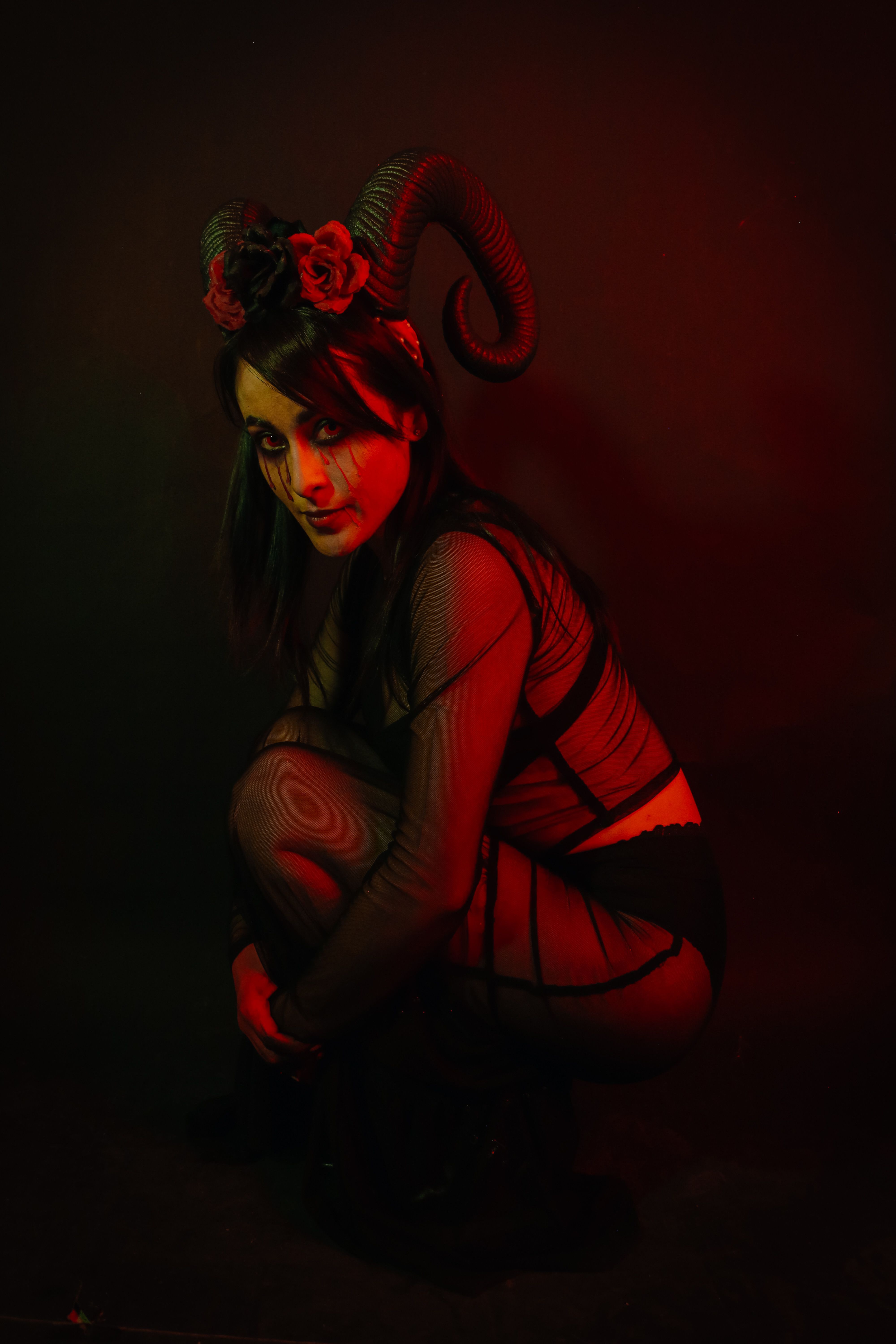 A woman in fantasy makeup and costume with horns in dark moody lighting.