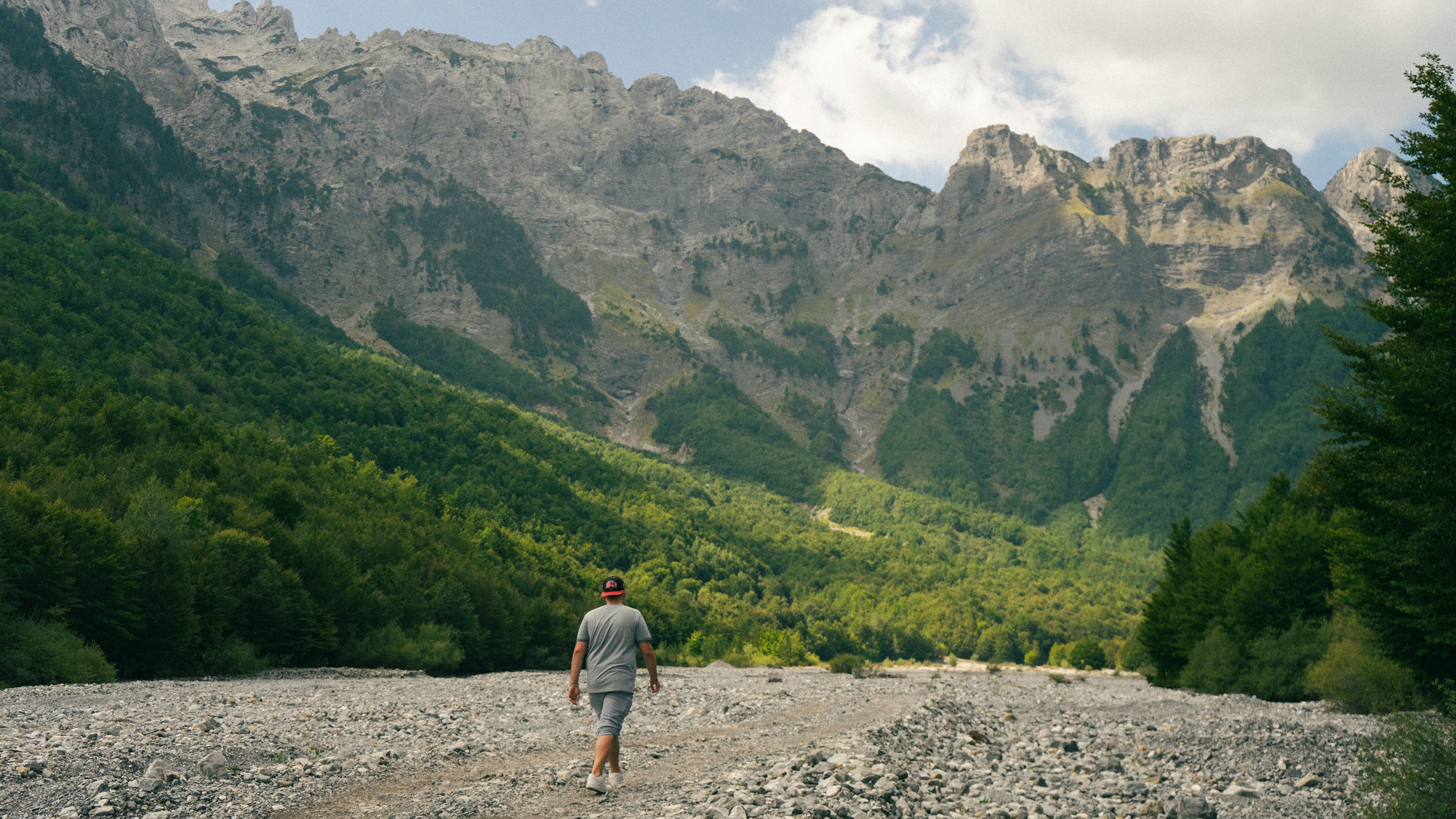 Person hiking in Valbonë Valley, Albania with stunning mountain backdrop.