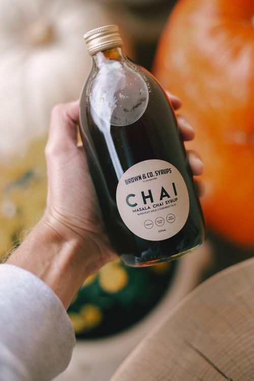 Free A person holds a bottle of Brown & Co. Masala Chai Syrup, perfect for creating chai lattes. Stock Photo