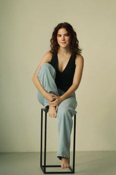Casual portrait of a woman sitting on a minimalistic stool indoors.