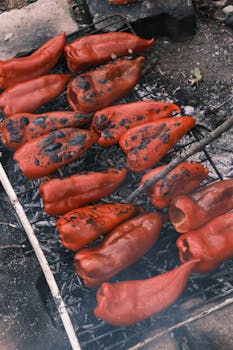 Charred red peppers cooking on a barbecue grill outdoors, showcasing rustic cooking style.