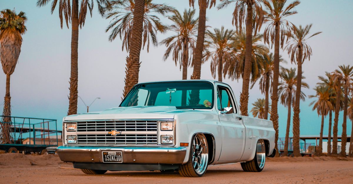 Vintage pickup truck parked under palm trees during a vibrant sunset, creating a nostalgic and warm atmosphere.