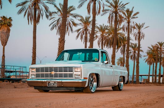 Vintage pickup truck parked under palm trees during a vibrant sunset, creating a nostalgic and warm atmosphere.