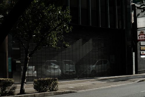 Free A quiet urban street with a modern building entrance and reflective shuttered doors. Stock Photo