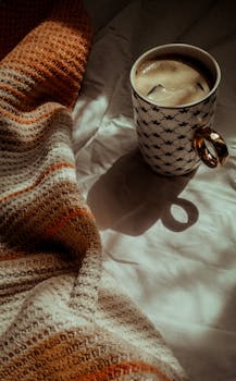 Warm and cozy morning with a steaming cup of coffee beside a colorful knit blanket in soft lighting.