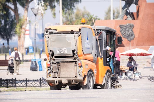 Street cleaning vehicle operating in a public park in İzmir, Türkiye, under bright sunlight.