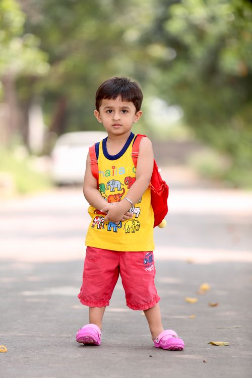 Free Adorable child wearing vibrant colors and backpack standing on a sunny path outdoors. Stock Photo