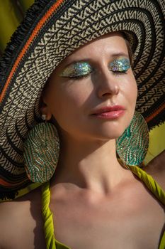 Glamorous portrait of a woman wearing a wide-brim hat and sparkling glitter makeup, epitomizing summer fashion.
