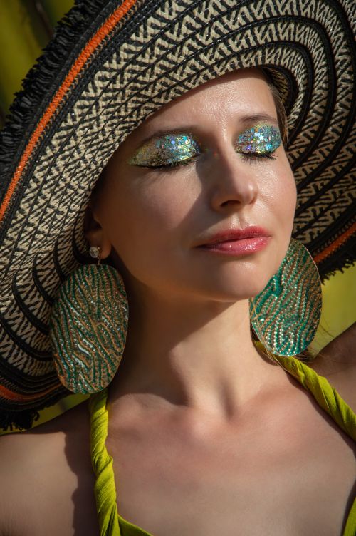 Free Glamorous portrait of a woman wearing a wide-brim hat and sparkling glitter makeup, epitomizing summer fashion. Stock Photo