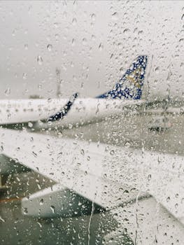 Blurry view of airplane wing and tail through rain-soaked window, Almaty airport.