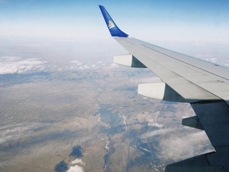 View of Kazakhstan's vast landscape from an airplane window, showcasing the country's plains and sky.