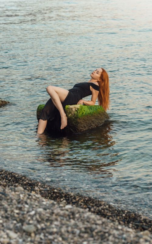 Free Woman in black dress relaxing on a mossy rock by the sea in Gagra. Stock Photo
