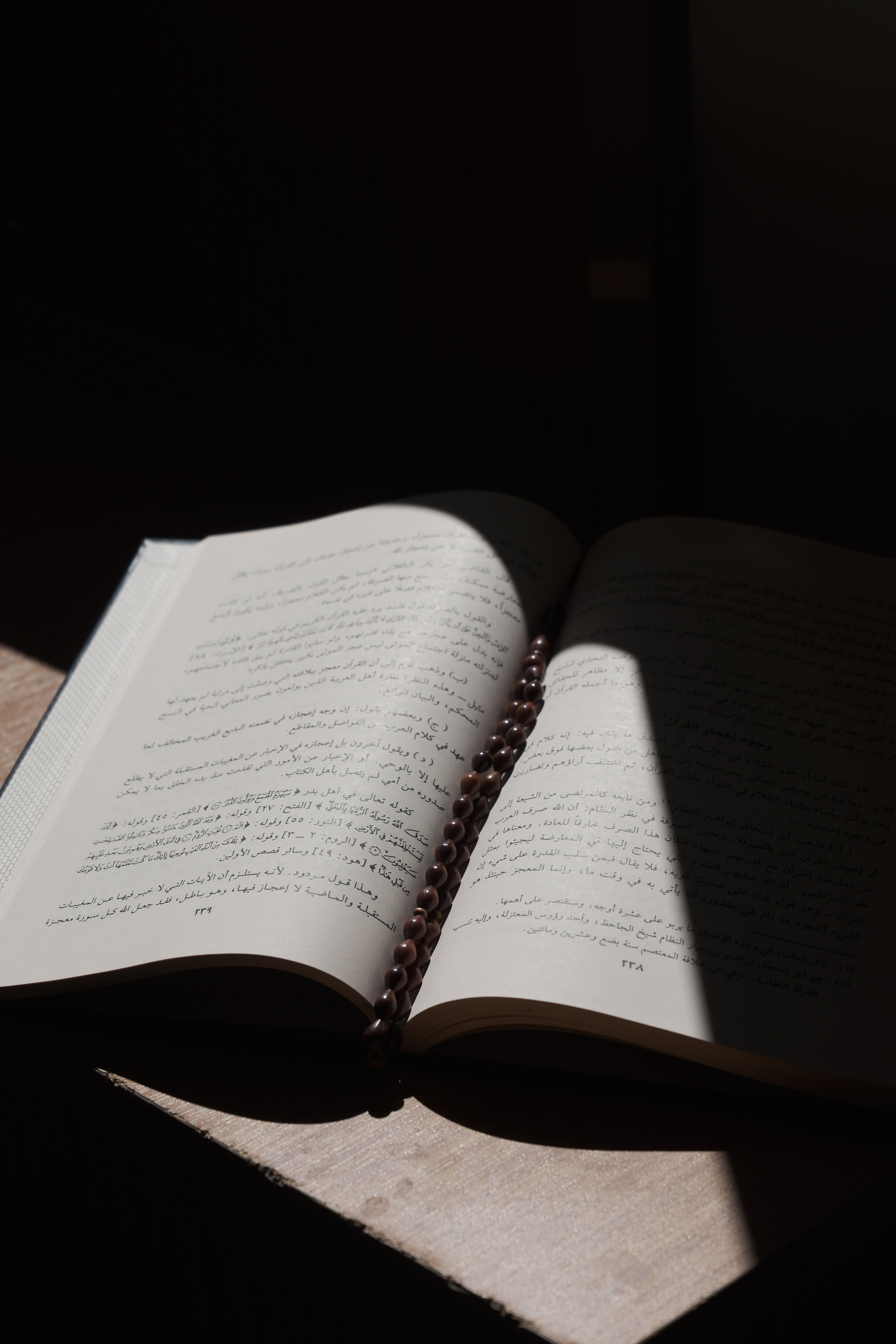 An open Quran with a rosary placed under soft, dramatic lighting.
