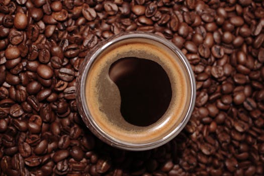 A close-up top view of an espresso cup surrounded by roasted coffee beans.
