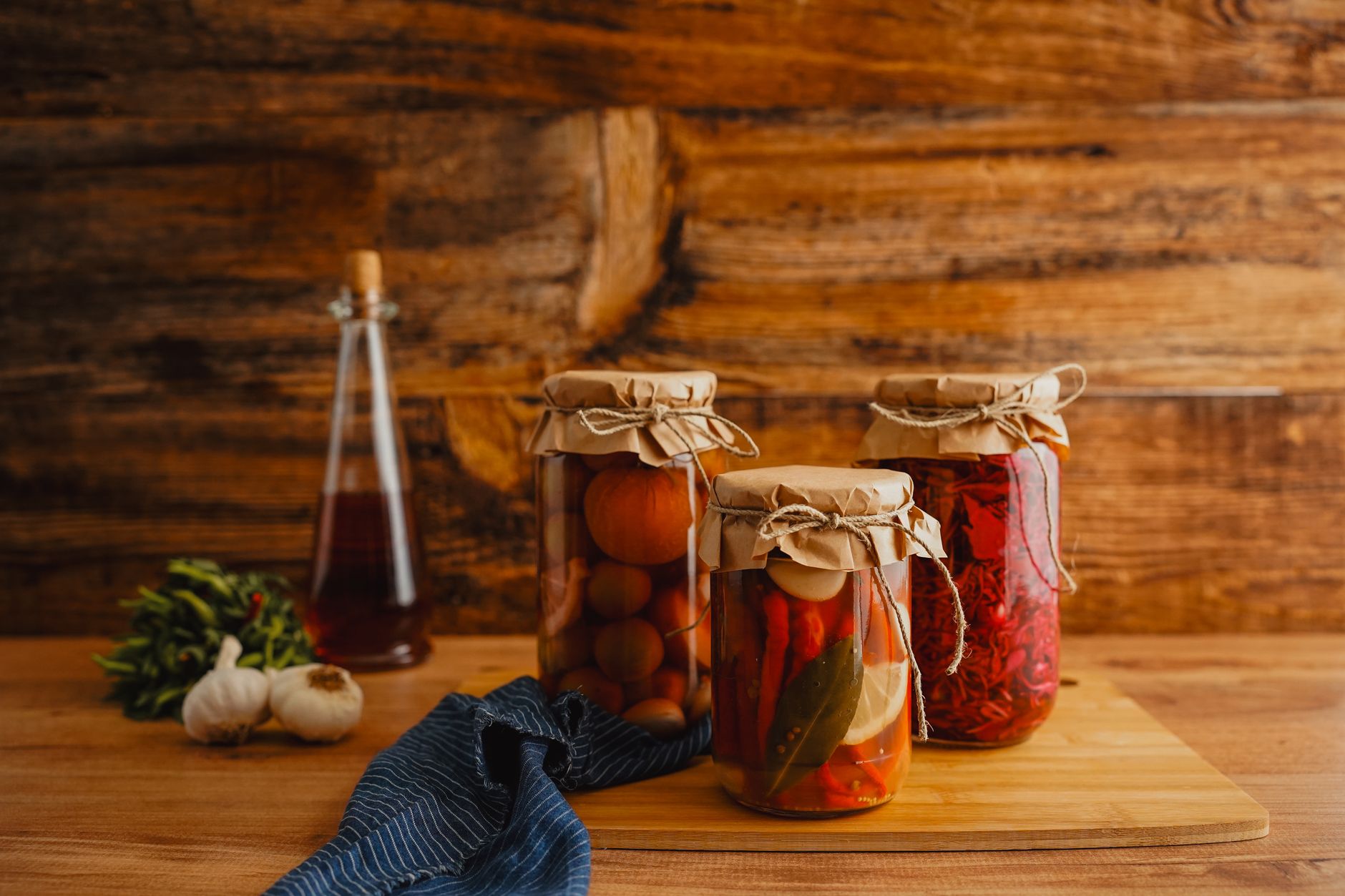 Vidros de vidro com pickles caseiros de legumes sobre bancada de madeira na luz da manhã
