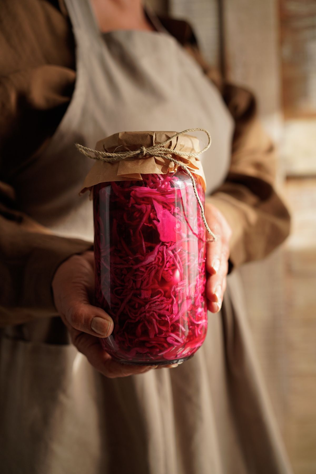 Hands holding a rustic glass jar of homemade fermented vegetables in a home kitchen