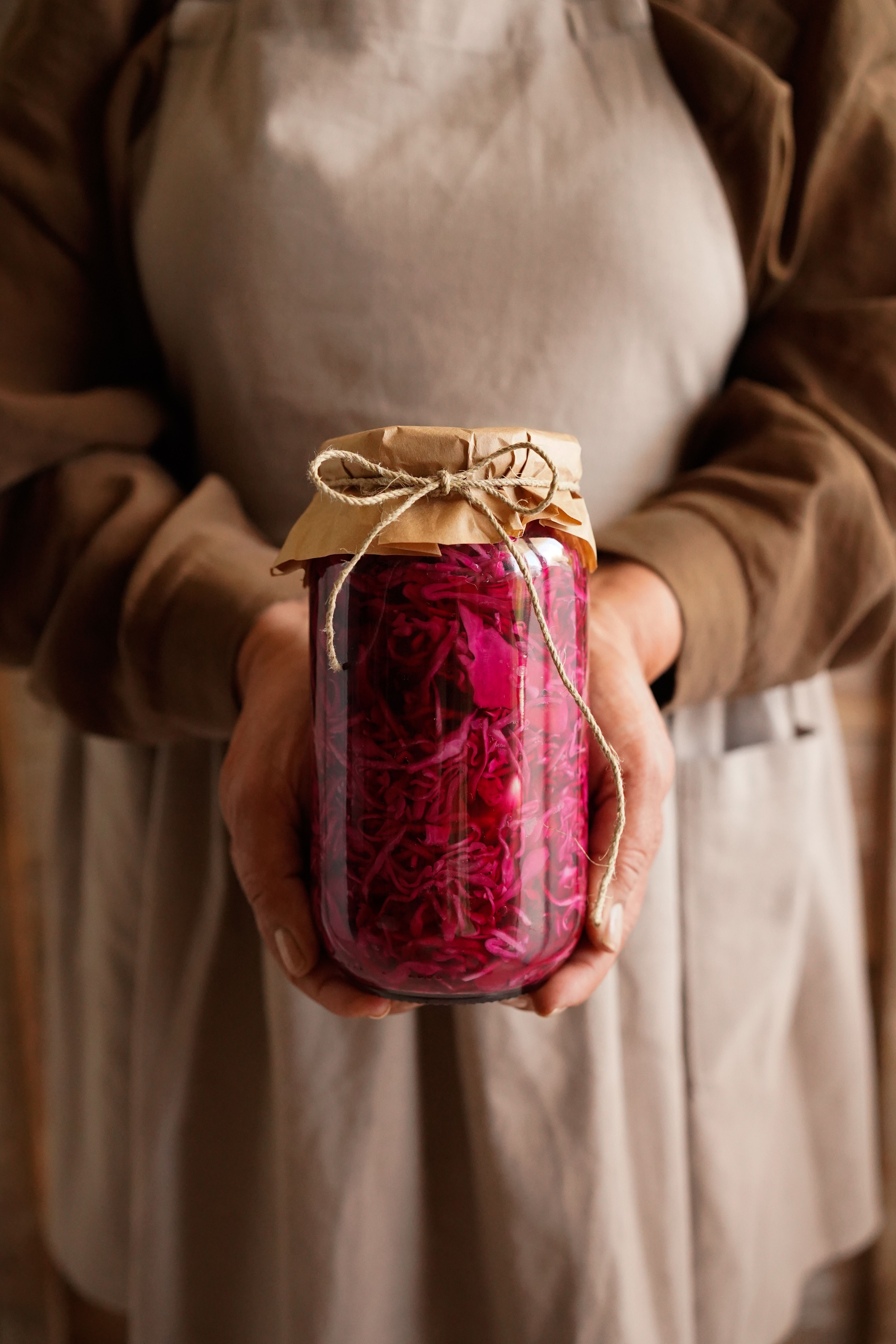 Hands holding a rustic jar filled with vibrant dried rose petals.