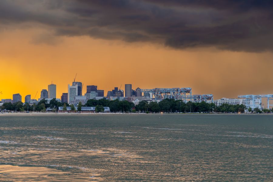 The Boston skyline seen across the harbor under a stormy orange sunset