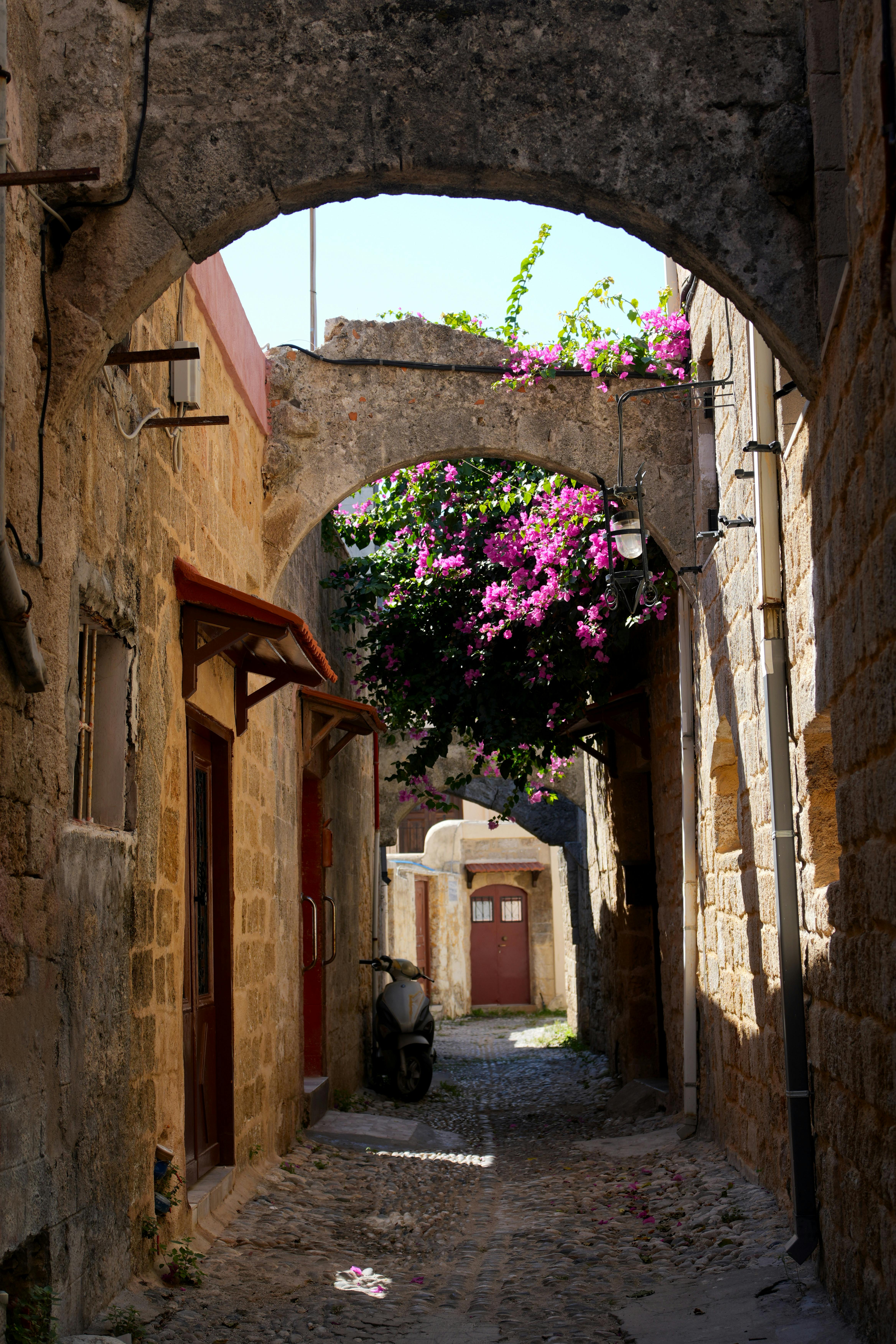 Charming cobblestone street with ancient arches and vibrant flowers in Rhodes, Greece.
