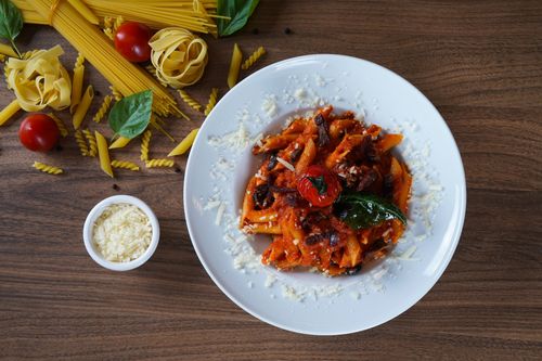 Free A plate of homemade pasta with a rich tomato sauce garnished with cheese, basil, and olives. Stock Photo