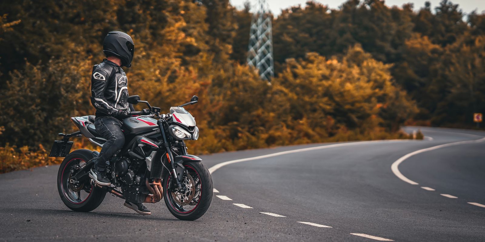 A motorcyclist paused on a road surrounded by fall foliage