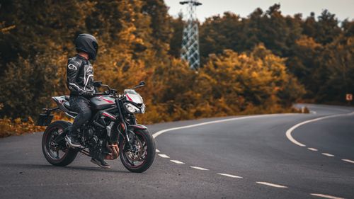 Free A biker on a motorcycle pauses on a deserted road surrounded by fall foliage. Stock Photo