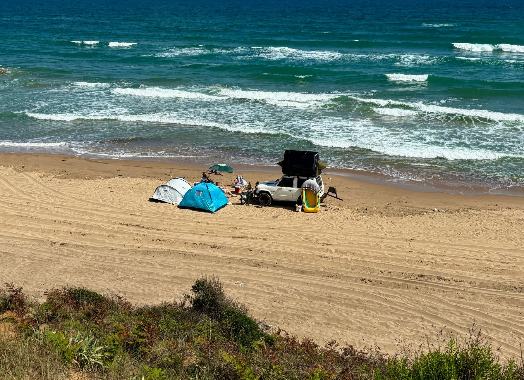 A beachside campsite with tents and vehicle access, which is the sort of setup where privacy, drainage and a dry place to change matter as much as the shower itself.