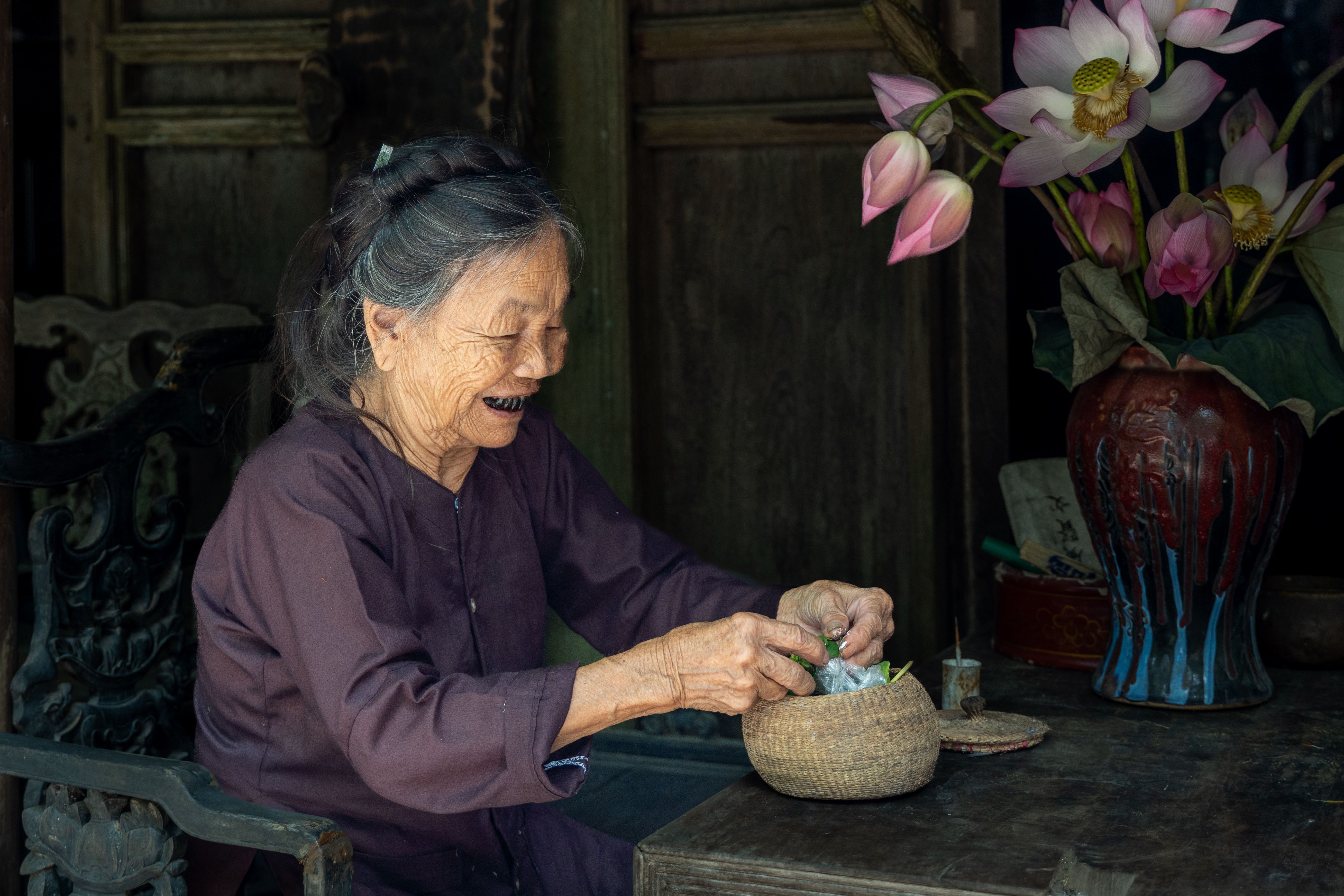 An elderly woman enjoying a moment in traditional Hanoi setting with lotus flowers.