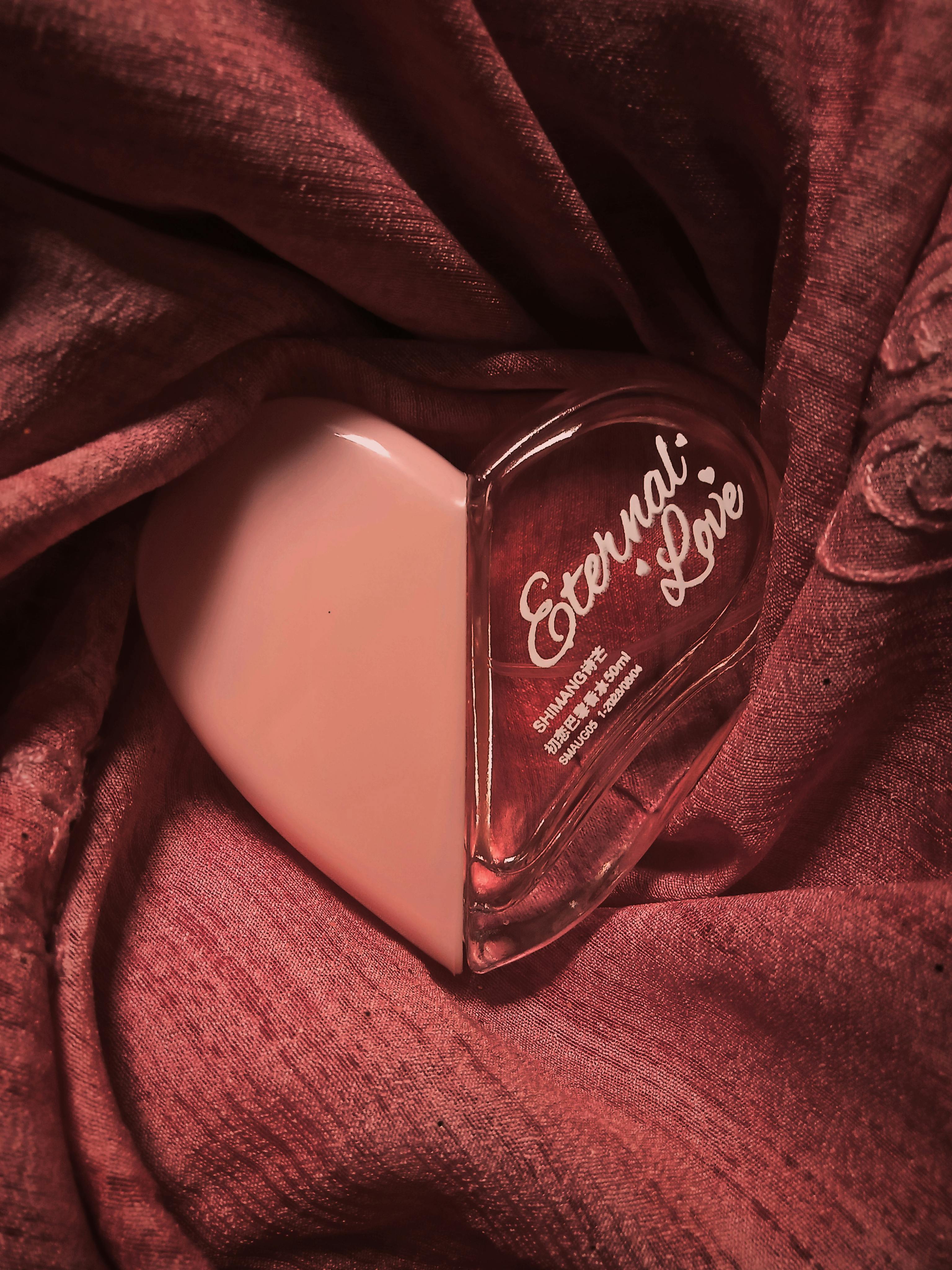 A heart-shaped perfume bottle labeled 'Eternal Love' resting on dark pink fabric, symbolizing romance.