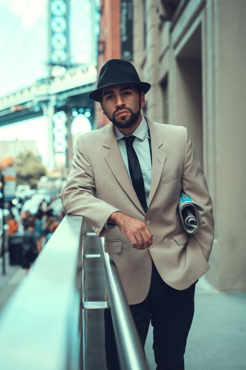 Free Dapper man in a suit and fedora leans on a NYC railing, exuding urban style. Stock Photo