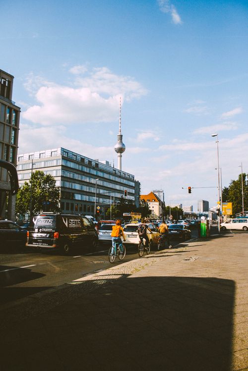 Free Dynamic city street scene in Berlin featuring parked cars, cyclists, and Fernsehturm tower. Stock Photo