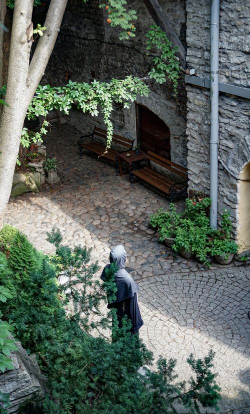 Free A peaceful courtyard in Tallinn featuring cobblestone paths, greenery, and a solitary figure. Stock Photo