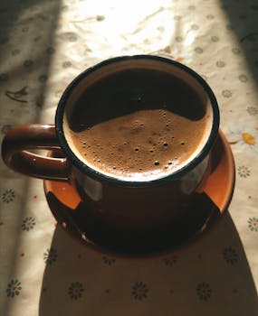 A warm cup of coffee in sunlight on a patterned tablecloth, perfect for cozy moments.