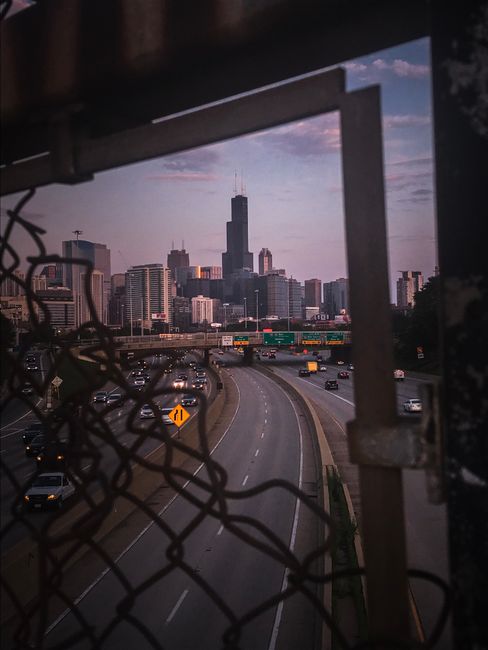 View of the Chicago skyline during dusk through a broken fence, capturing urban life.