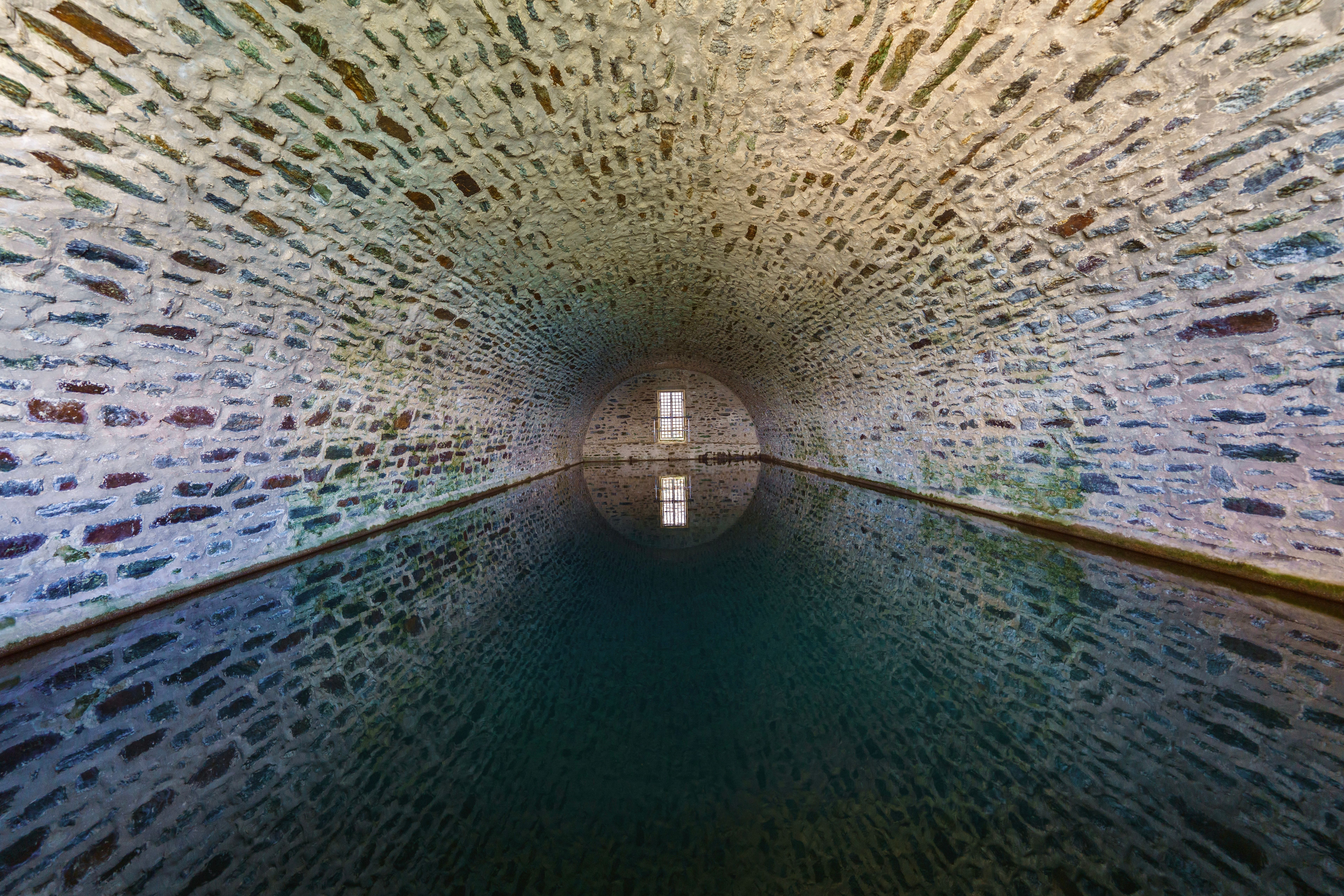 Symmetrical view of a stone tunnel with tranquil water reflection.