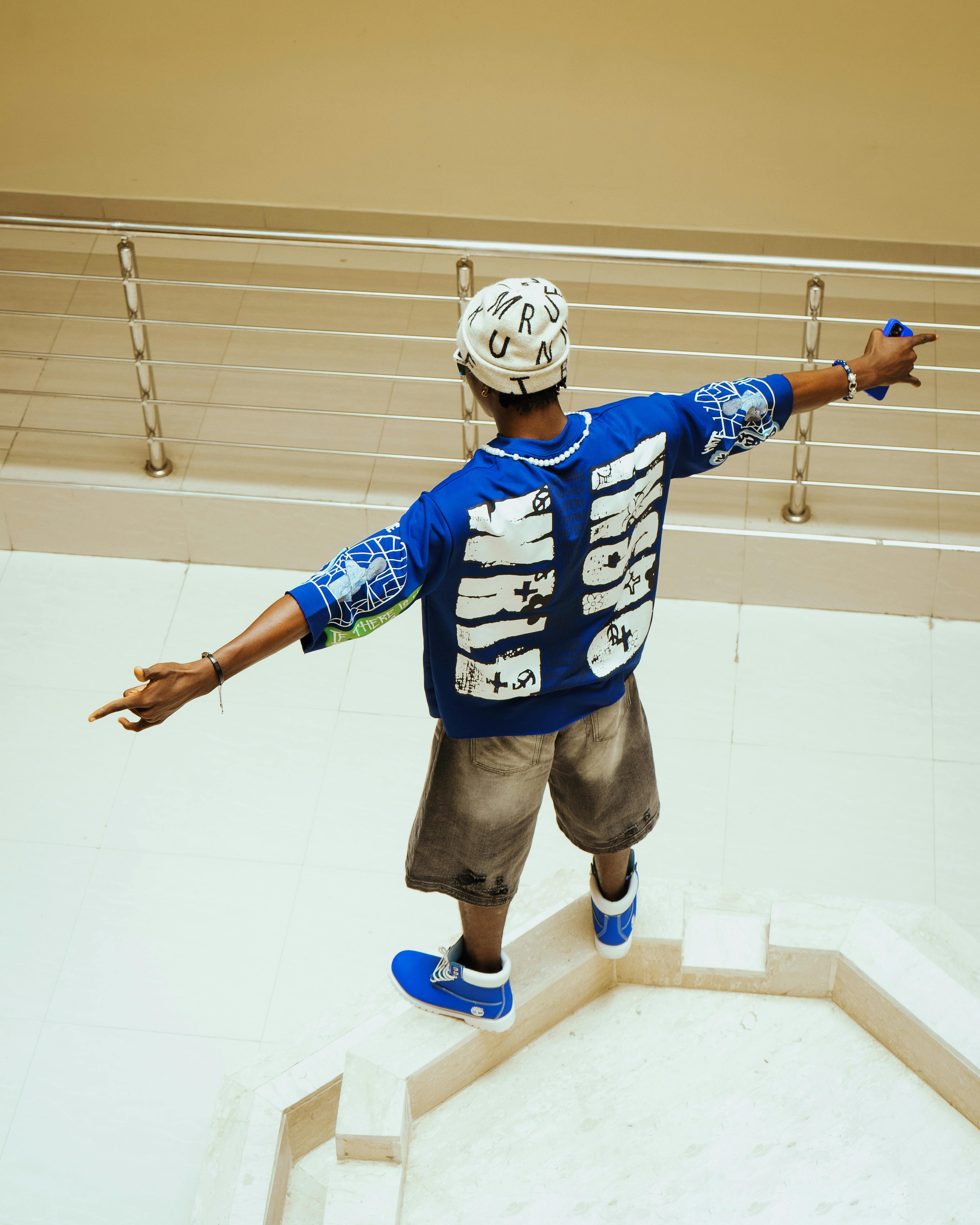 Young adult male in urban clothing with arms outstretched indoors.
